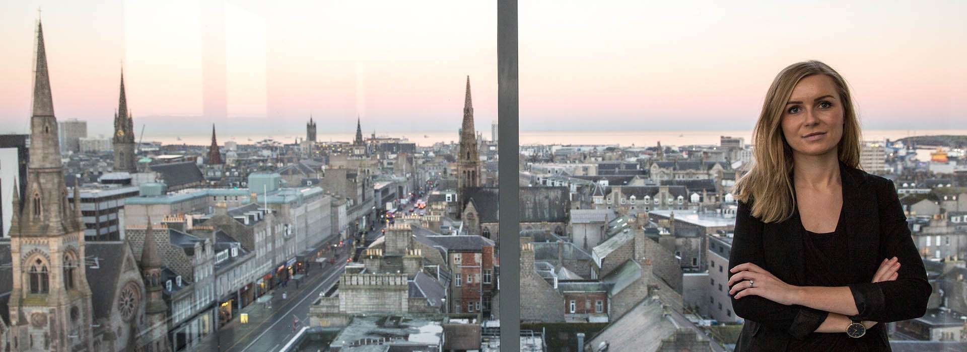 woman standing at window with Aberdeen City skyline in view