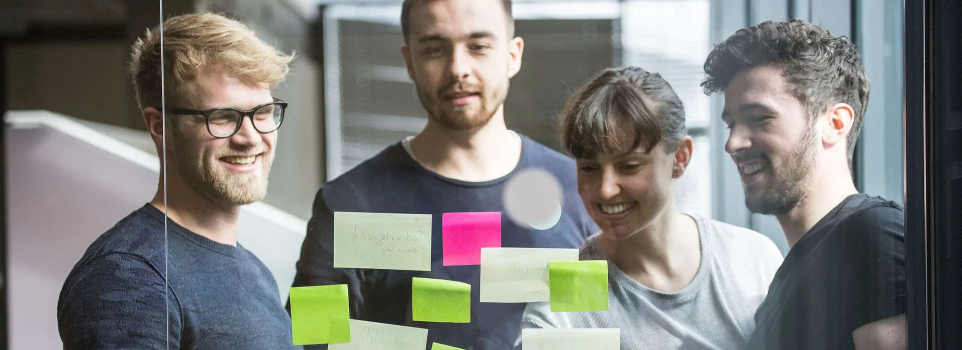 a group of people looking at post it notes on a glass wall