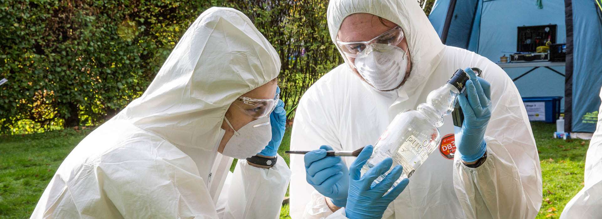 two people in forensic suits dusting a bottle for prints