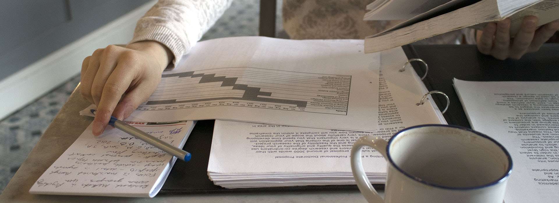 person holding pen over folder of documents
