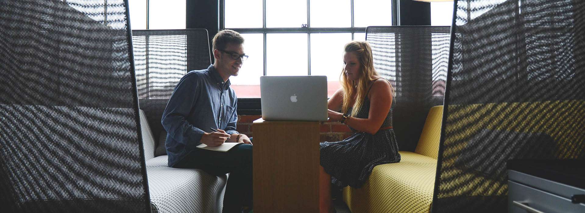 two people sitting in a booth looking at a laptop