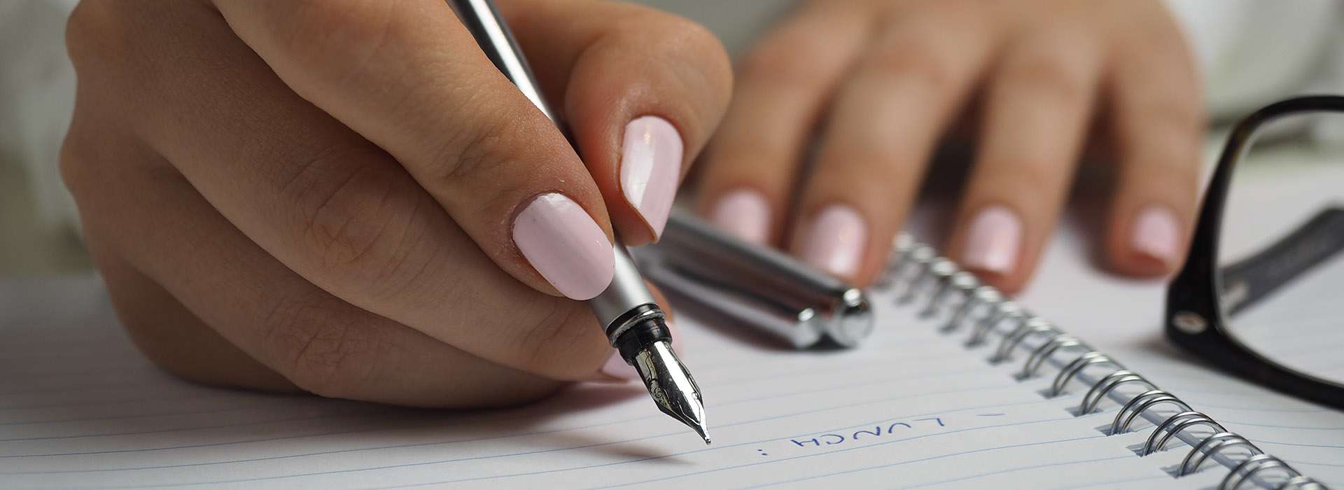 person with painted nails writing in a notebook