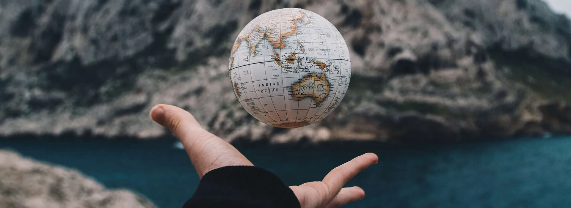 hand throwing a globe against a mountain background