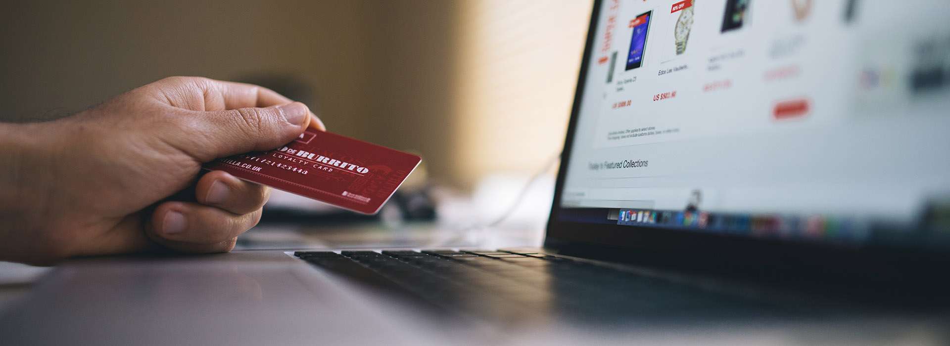hand holding credit card next to laptop