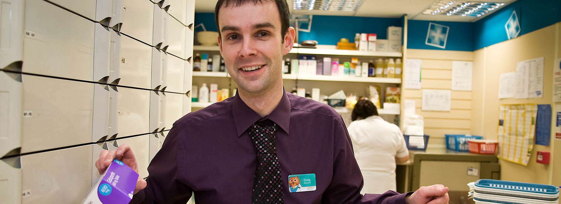 man in pharmacy showing a box of medicine to the camera