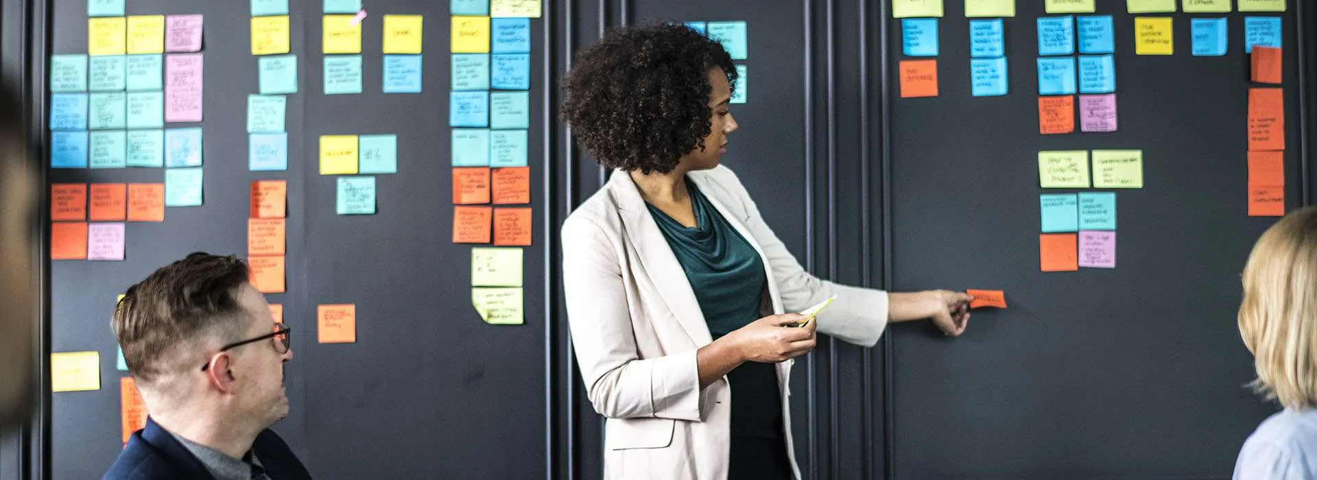 People in a business setting using post-it notes on a blackboard wall