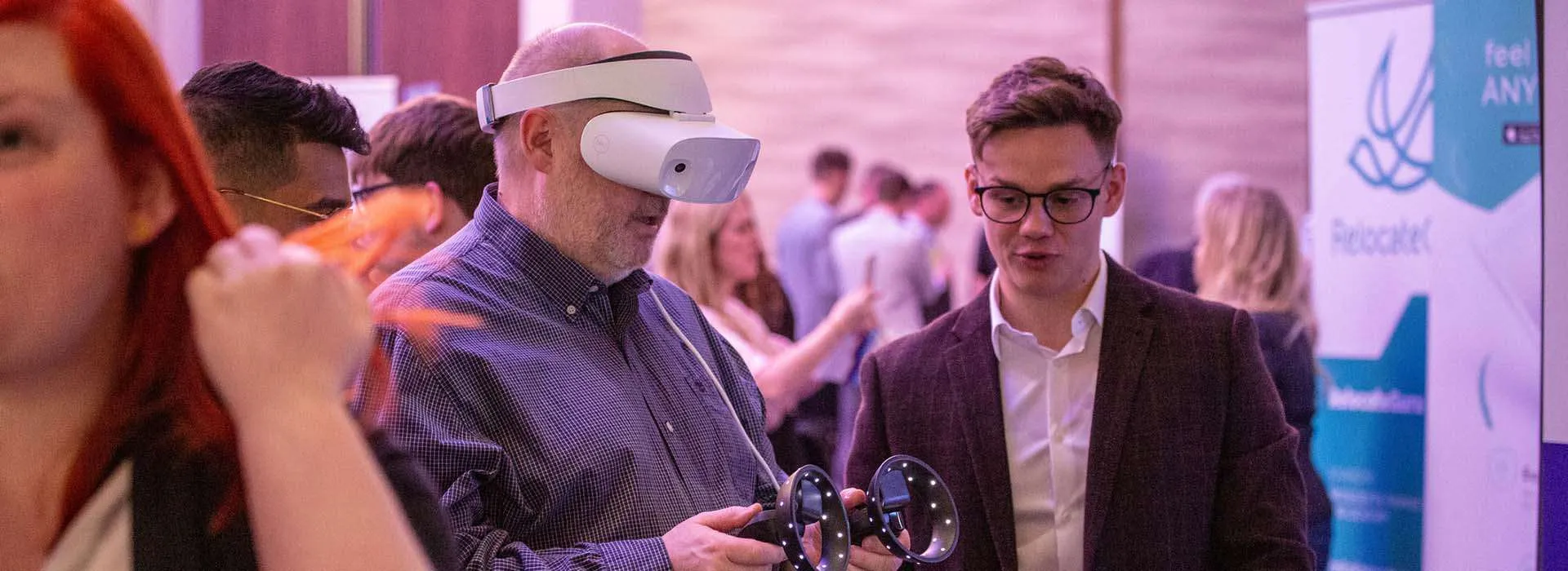 two people at an event, one is using a vr headset and controller