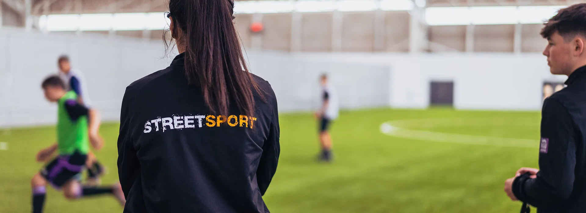 Football training with a person in the foreground wearing a jacket with 'Streetsport' on the back