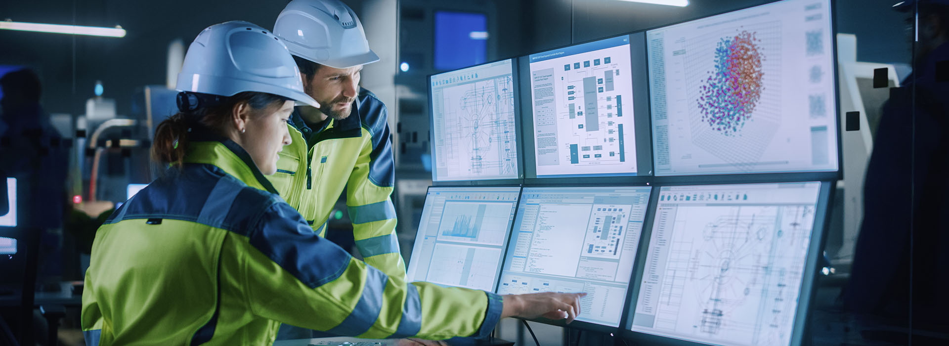 two people in yellow hi-vis jackets and hard hats are looking at a large bank of computer screens