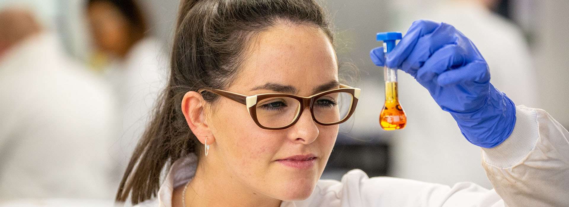 woman wearing protective gloves looking closely at a flask