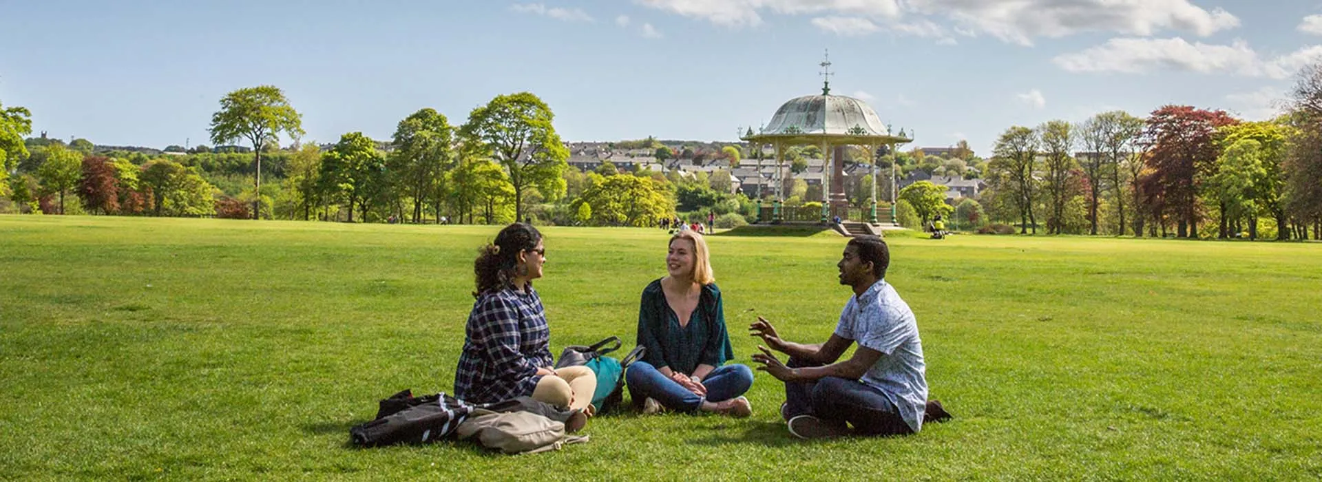three people sitting in grass in Duthie Park Aberdeen