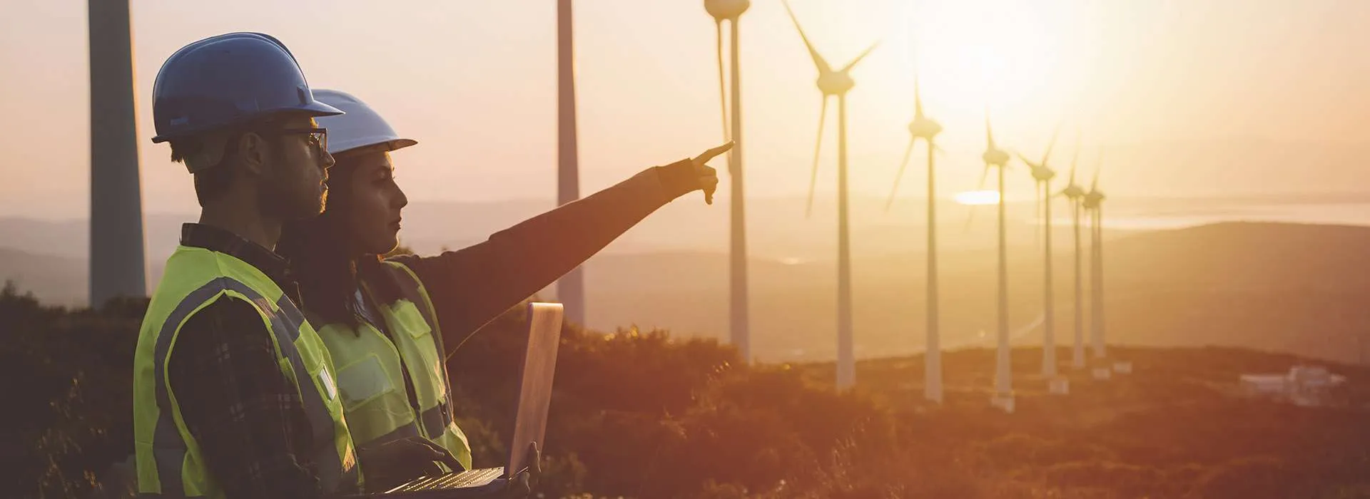 two people in helmets and high vis looking out over a wind farm