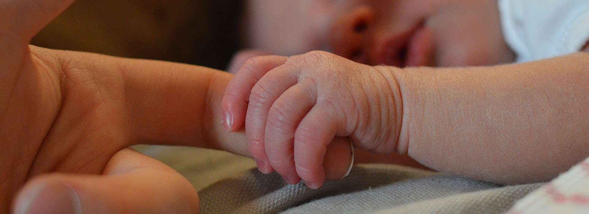 newborn baby holding an adult finger