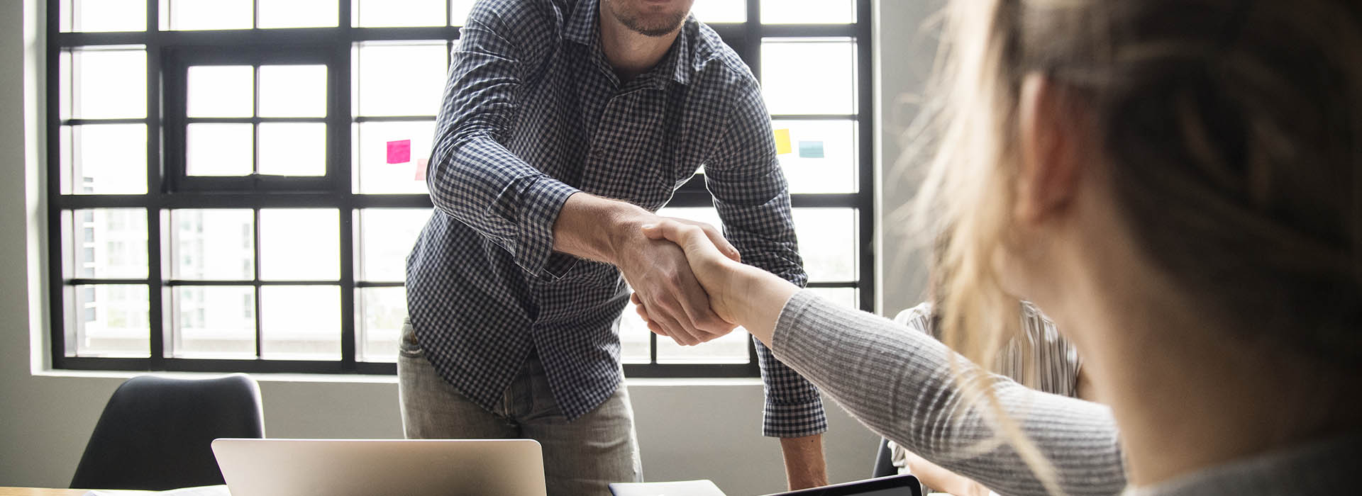 two people shake hands over their laptops on a table