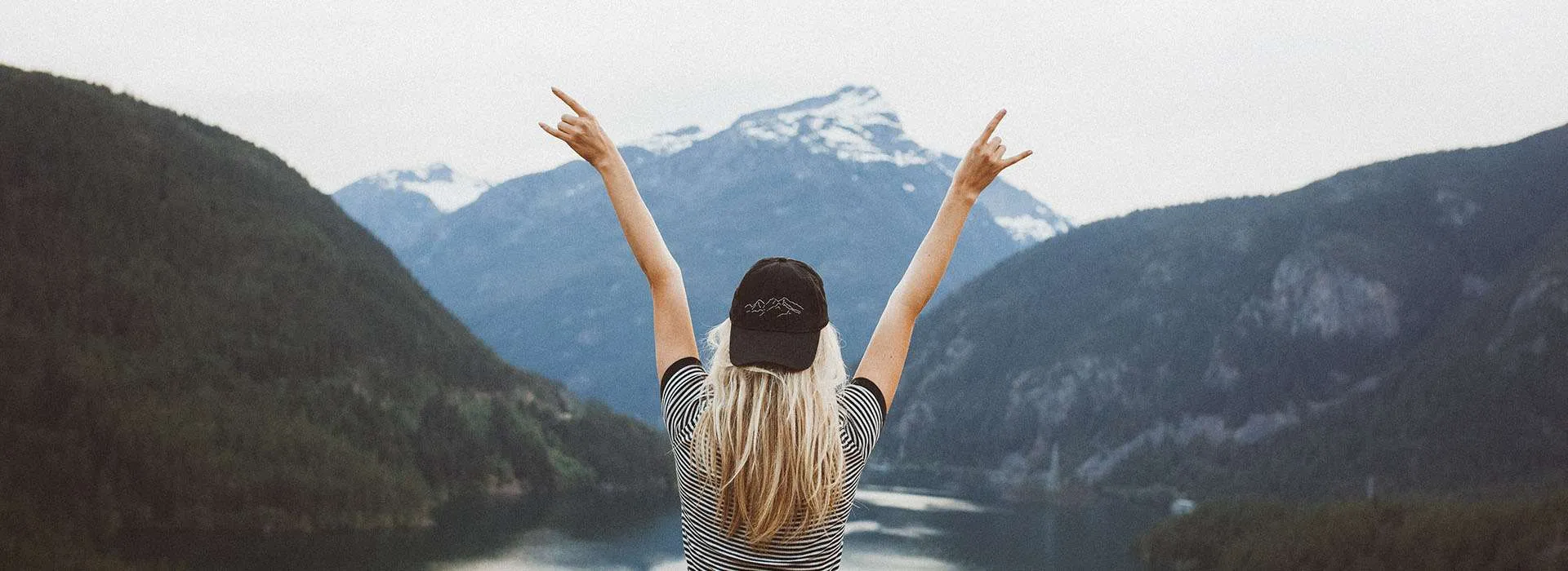 a woman holding her hands up in celebration in front of a mountainous vista