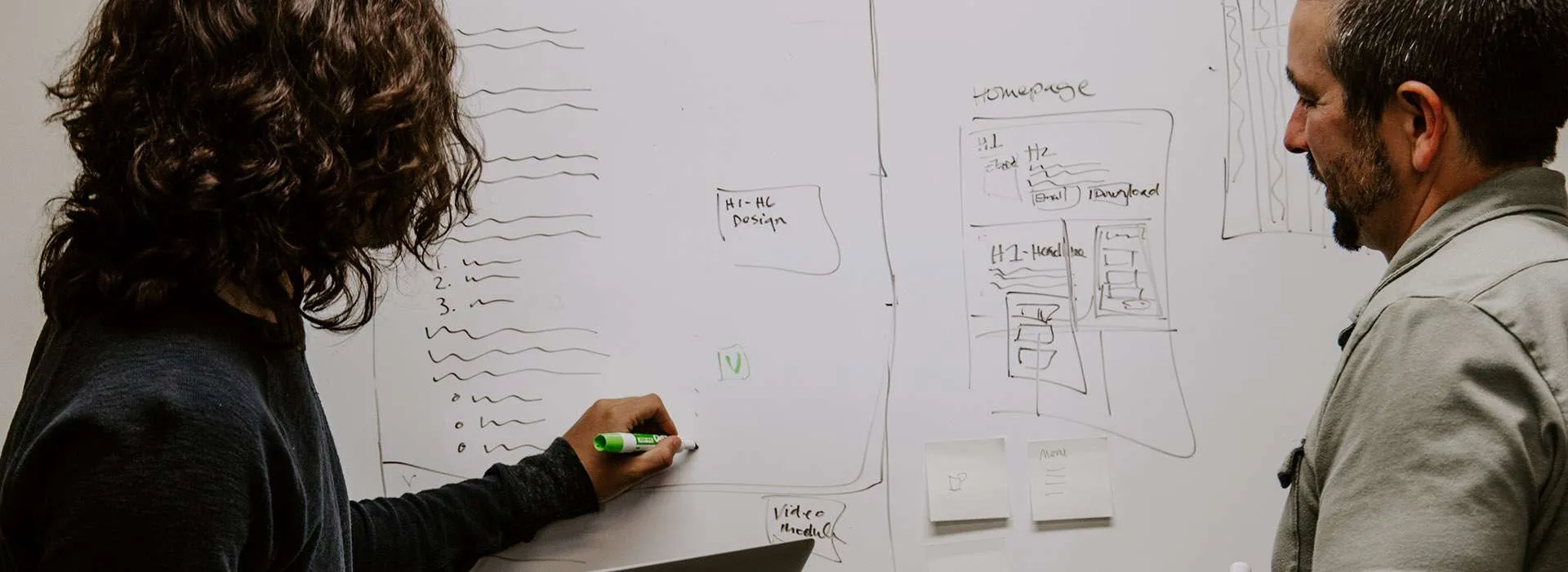 person holding a laptop and writing on a whiteboard
