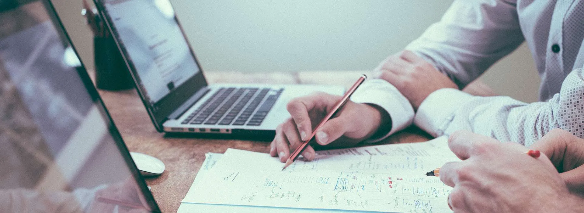 two people sitting with their laptops reviewing a paper document