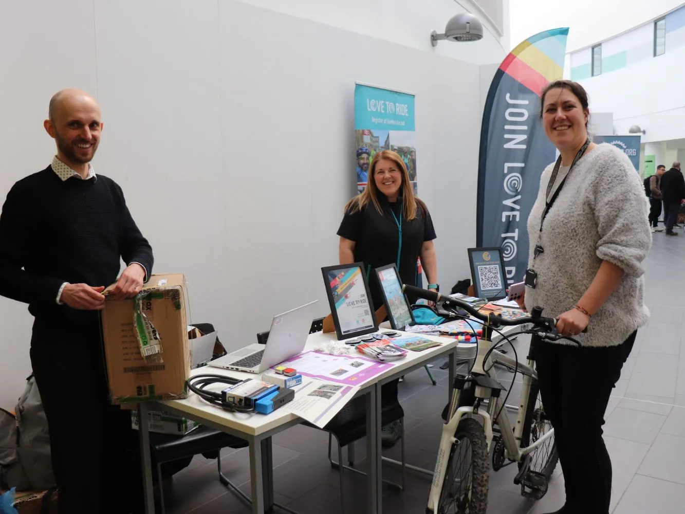 Three RGU staff members at a stall in the Sir Ian Wood Building with one holding a bike