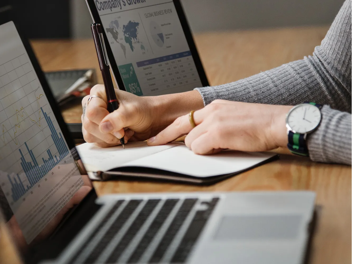 person writing in notebook next to laptop