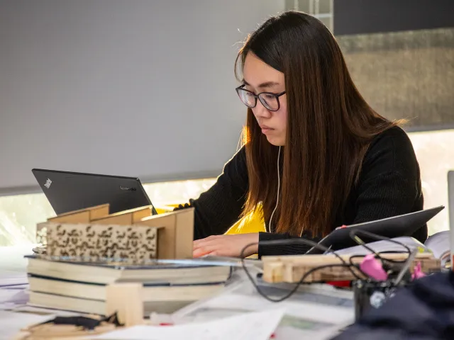student looking at laptop next to an architectural model