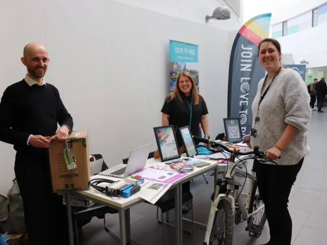 Three RGU staff members at a stall in the Sir Ian Wood Building with one holding a bike