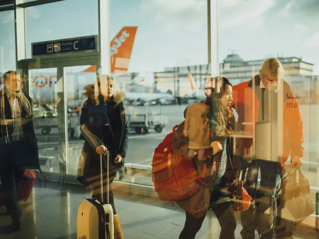 people in reflected in an airport window with planes in the background