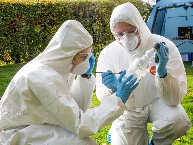 two people in forensic suits dusting a bottle for prints