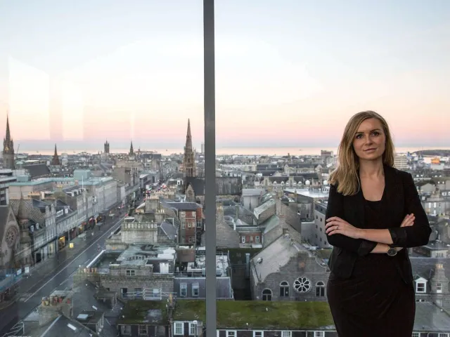 woman standing at window with Aberdeen City skyline in view