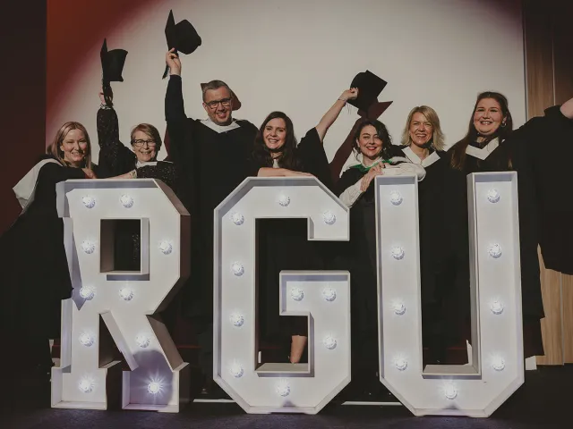 7 graduates pose for photo by giant RGU letters at P&J Live
