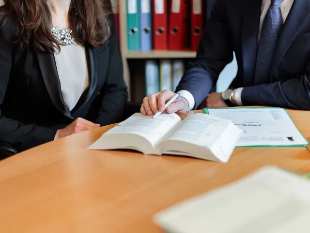 two professional people pointing at a book with a pen