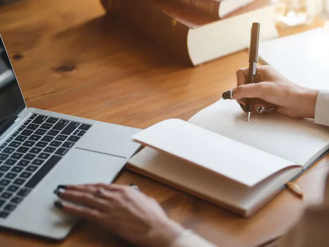 Person writing with a laptop nearby