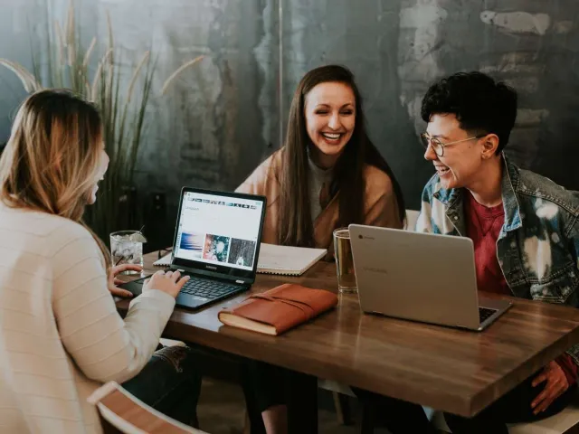 students laughing at a table with laptops