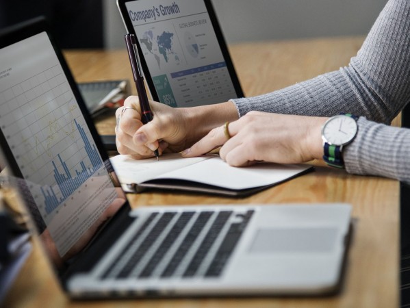 someone taking notes next to screens with graphs