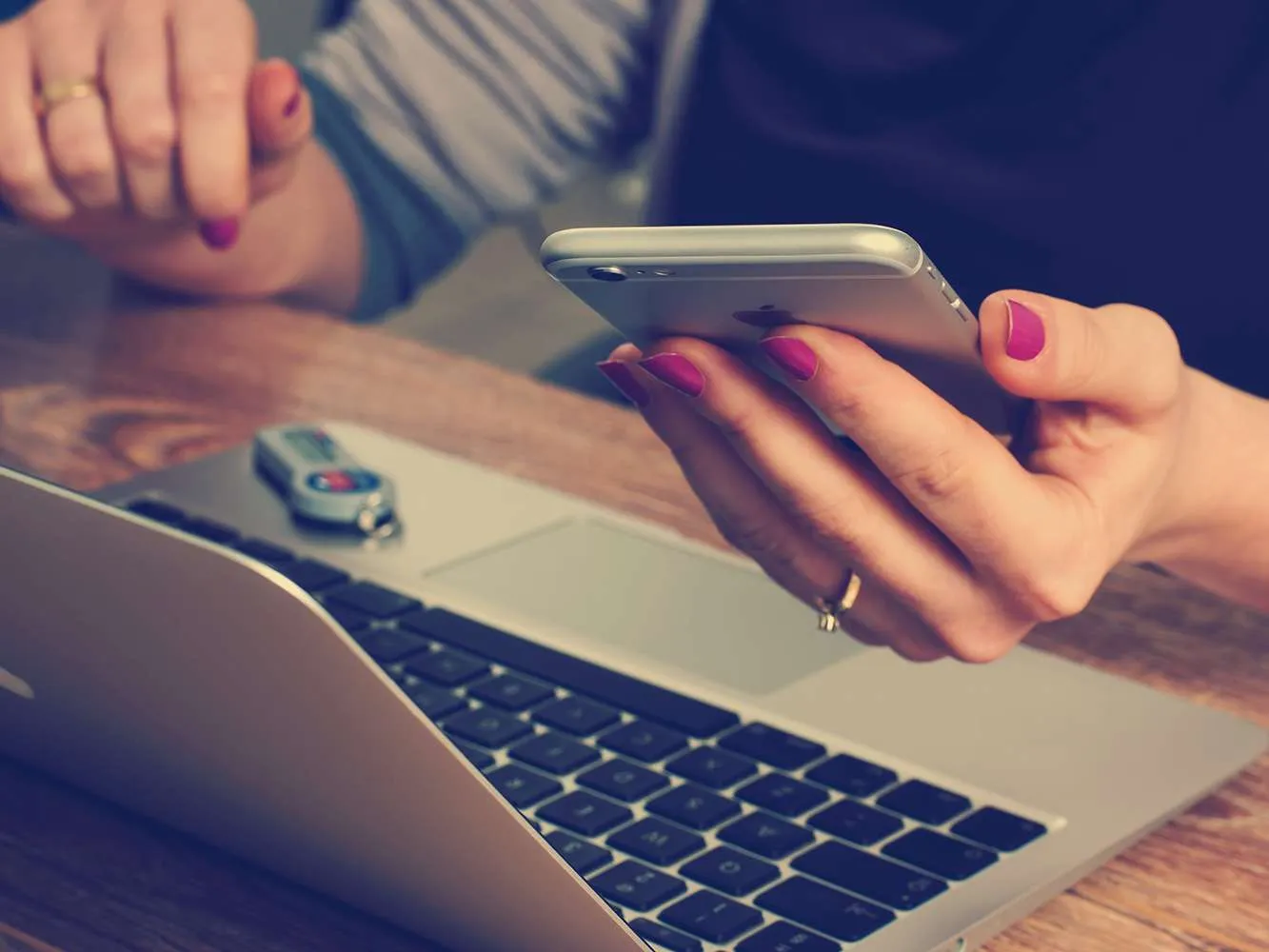 woman holding phone next to computer